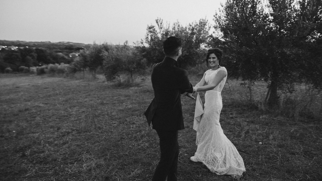 Coppia di sposi che si tengono per mano e sorridono durante un momento spontaneo in campagna al tramonto &ndash; fotografia di matrimonio in stile reportage