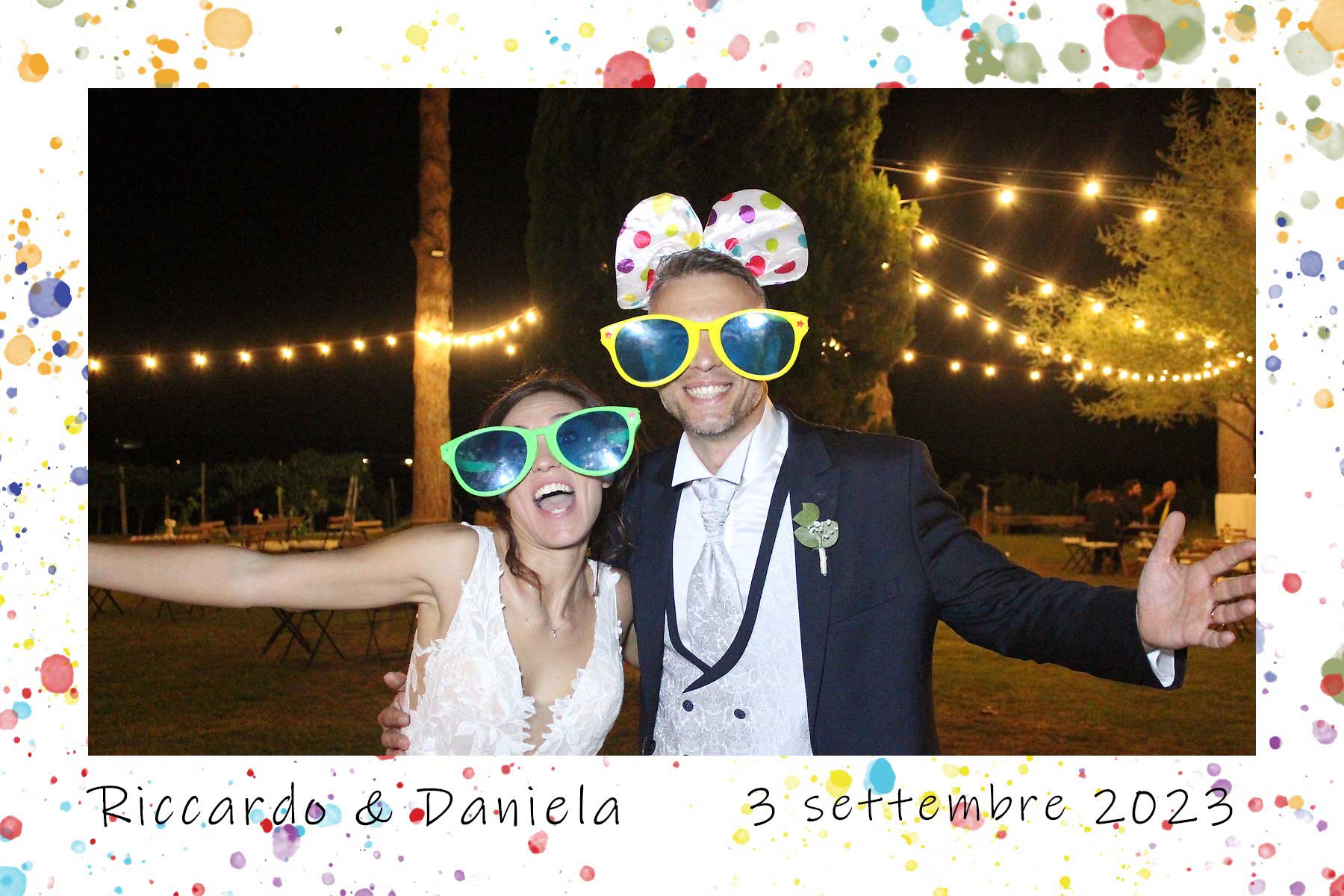 Sposi divertiti con occhiali e accessori colorati al photo booth Fatti un Selfie durante un matrimonio serale